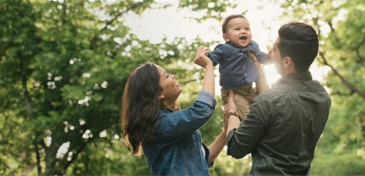 A women and man holding a baby up in the air in a park