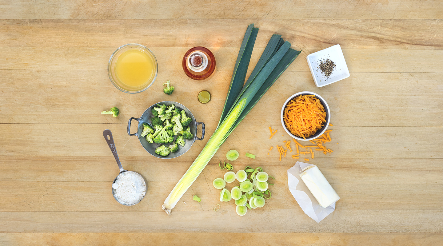 Ingredients for Cheesy Broccoli Leek Soup on a wooden countertop