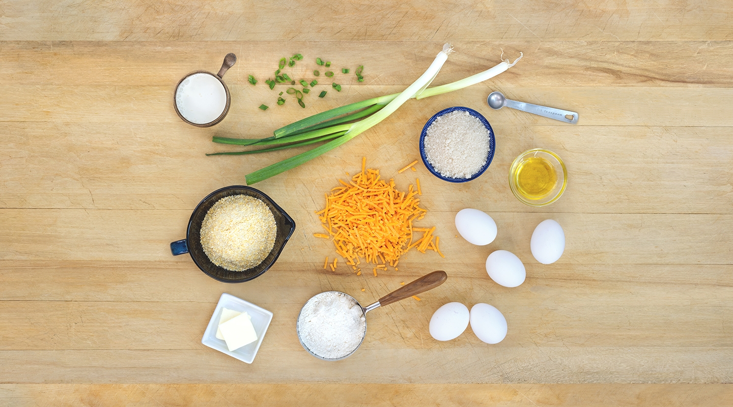 Ingredients for Cheesy Cornbread Muffins on a wooden countertop