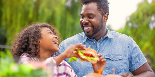 A daughter and father share a moment while eating a sandwich at a picnic