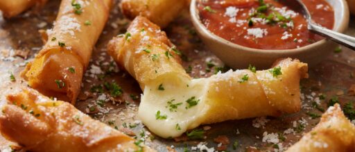 Crispy Mozzarella String Cheese Rolls on a wooden cutting board with a bowl of marinara sauce